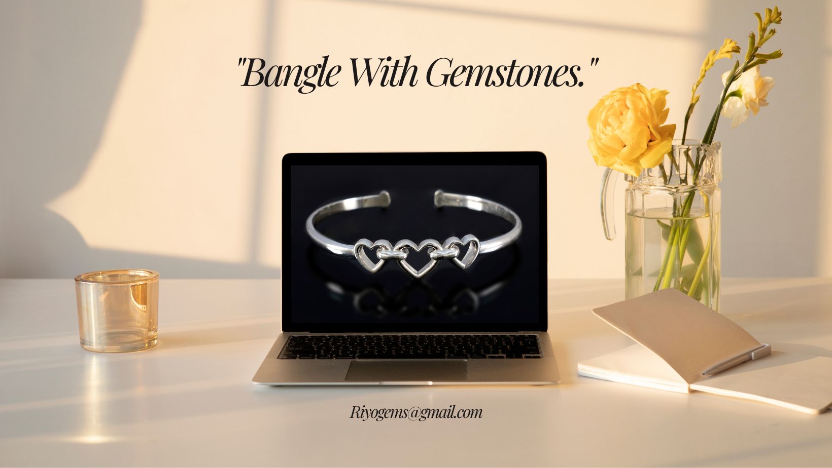 Stylish bangle with gemstones displayed on a laptop with a flower vase and notebook